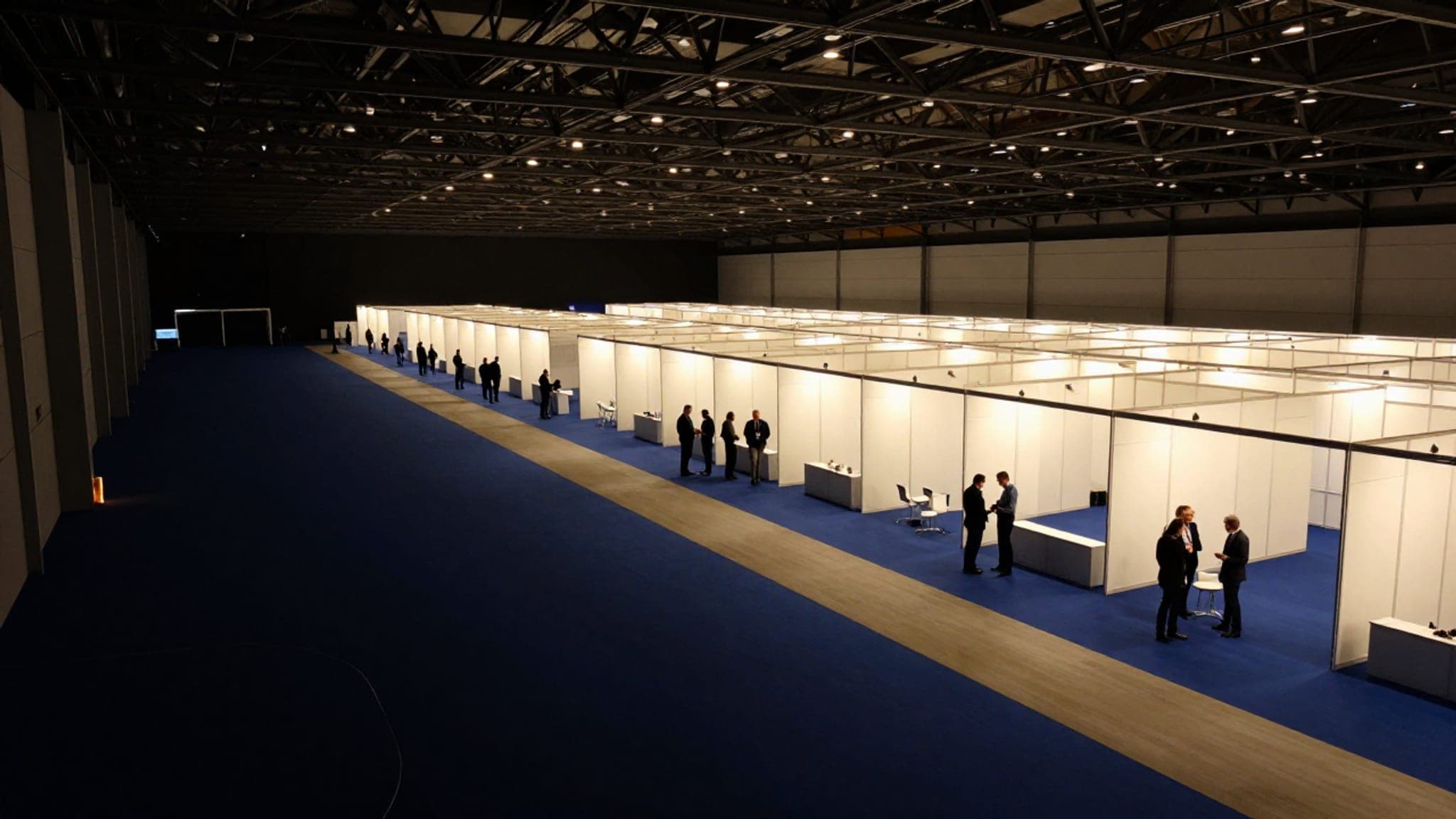 Rows of lit exhibition booths laid out in a grid across the blue carpet of a dark trade show hall